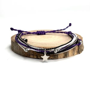 Peut inclure: Un bracelet multi-brins avec des cordons violets, blancs et noirs, des perles argentées et un charme étoile argenté.