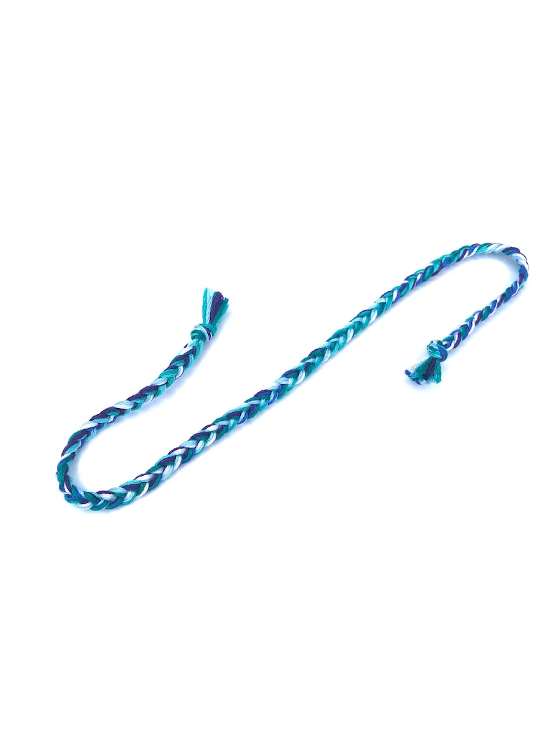 Puede incluir: Un cord&oacute;n trenzado con hilos azules, verdes y blancos. El cord&oacute;n est&aacute; atado en ambos extremos.