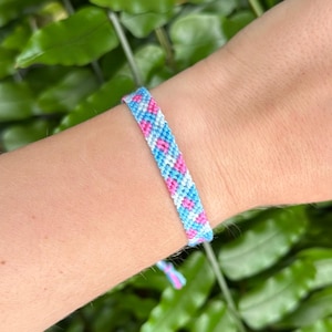 Può includere: Un braccialetto dell'amicizia intrecciato nei toni del blu, rosa e bianco. Il braccialetto presenta un motivo ripetuto a forma di diamante. Il braccialetto è legato con fili blu e rosa.
