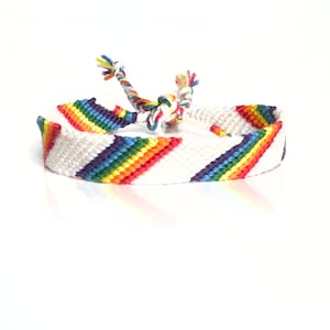 May include: White friendship bracelet with a diagonal rainbow stripe pattern. The bracelet is made of woven string.