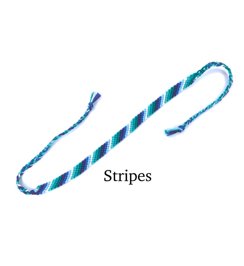 Puede incluir: Un brazalete de amistad azul, blanco y verde con la palabra "Stripes" impresa debajo.