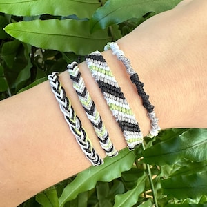 Op de afbeelding: Vijf vriendschapsarmbanden in zwart, wit en groen. De armbanden zijn geweven met een chevron-patroon en een gevlochten patroon.