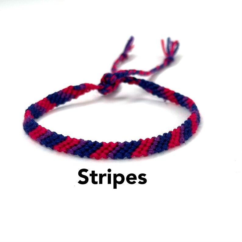 May include: A friendship bracelet with blue, pink, and purple stripes. The bracelet is tied in a knot and has long ends. The word "Stripes" is written below the bracelet.