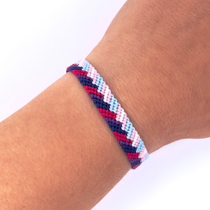 Peut inclure: Un bracelet d'amitié tissé avec un motif en chevron rose, bleu, blanc et bleu foncé.
