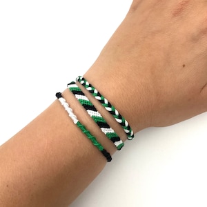 Op de afbeelding: Vier vriendschapsarmbanden in groen, zwart en wit. De armbanden zijn geweven met een chevron-patroon.