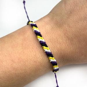 May include: A purple, black, white and yellow friendship bracelet with a diagonal pattern.