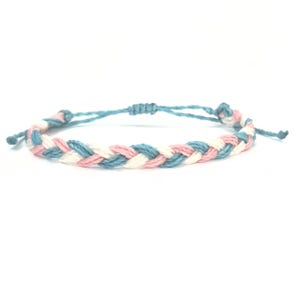 Puede incluir: Un brazalete de amistad trenzado con hilos azules, blancos y rosas.