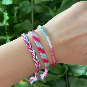Pode incluir: Três pulseiras de amizade em rosa, azul e branco. As pulseiras são tecidas com um padrão chevron e um padrão trançado.
