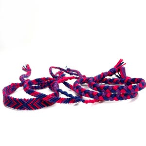 May include: A set of four friendship bracelets in pink and purple with a braided design.