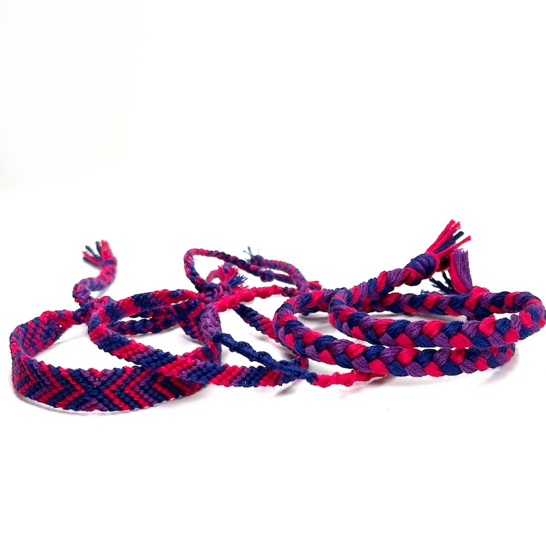 May include: A set of four friendship bracelets in pink and purple with a braided design.