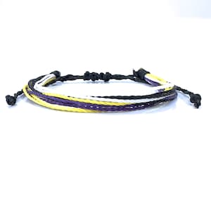 May include: A multi-coloured friendship bracelet with yellow, white and purple threads woven together. The bracelet is tied with a black cord.