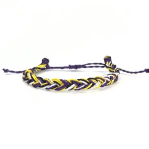 May include: A braided friendship bracelet with purple, yellow, white, and black threads.