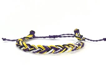 May include: A braided friendship bracelet with purple, yellow, white and black threads.