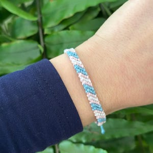 May include: A blue and pink friendship bracelet with a diagonal pattern.