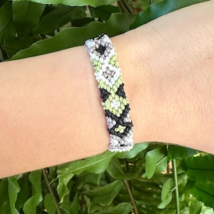 May include: A black, white and green friendship bracelet with a geometric pattern.