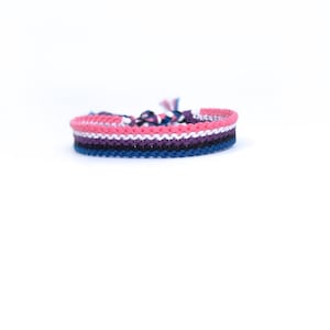 May include: A multi-coloured friendship bracelet with pink, white, purple, black and blue stripes.