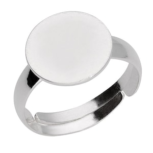 Op de afbeelding: Een zilverkleurige verstelbare ring met een groot, rond, leeg vlak. De band van de ring is gesplitst en gebogen, waardoor de maat kan worden aangepast. Het vlak van de ring is glad en reflecterend, geschikt voor graveren of personalisatie.