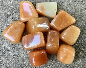 May include: A collection of ten tumbled carnelian stones in various shades of orange and yellow. The stones are smooth and polished, with a natural, earthy look.