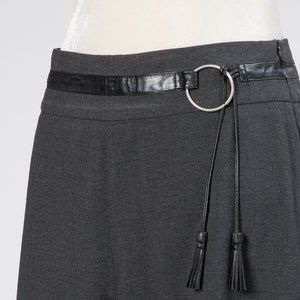 May include: A dark gray skirt with a black leather belt and a silver ring detail. The belt has two black tassels.