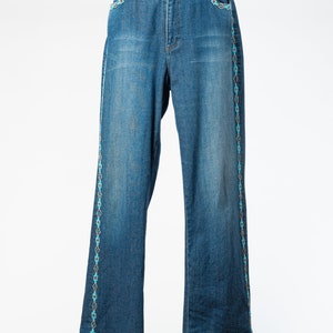 May include: Blue denim jeans with a turquoise and white embroidered design along the sides.