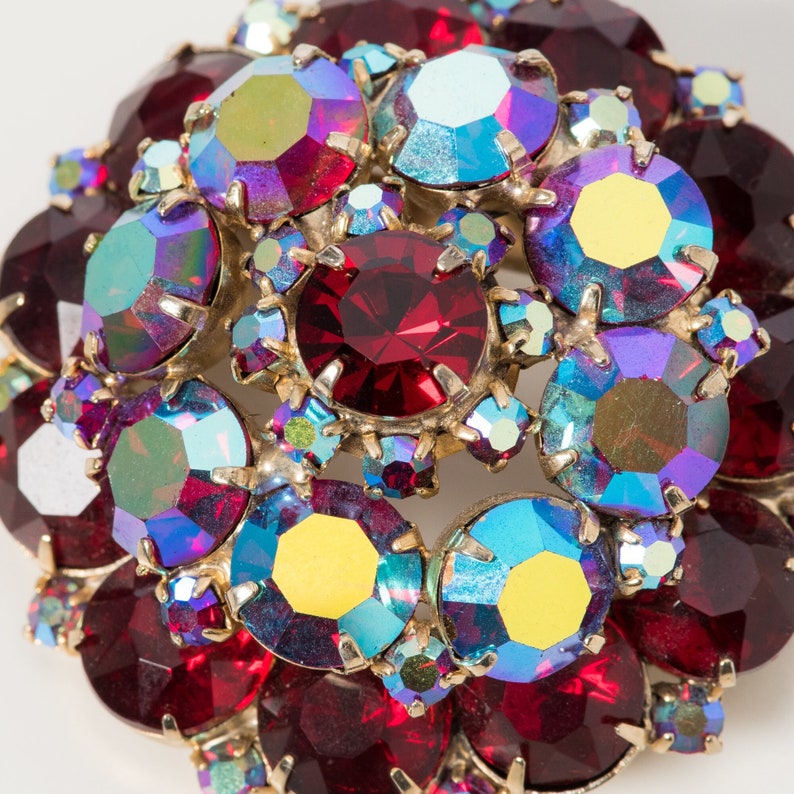 Puede incluir: Primer plano de un broche vintage con un grupo de piedras de imitaci&oacute;n rojas, azules e iridiscentes. Las piedras de imitaci&oacute;n est&aacute;n engastadas en metal dorado.