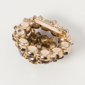 Puede incluir: Un broche dorado con un dise&ntilde;o circular adornado con piedras de imitaci&oacute;n rojas y azules.