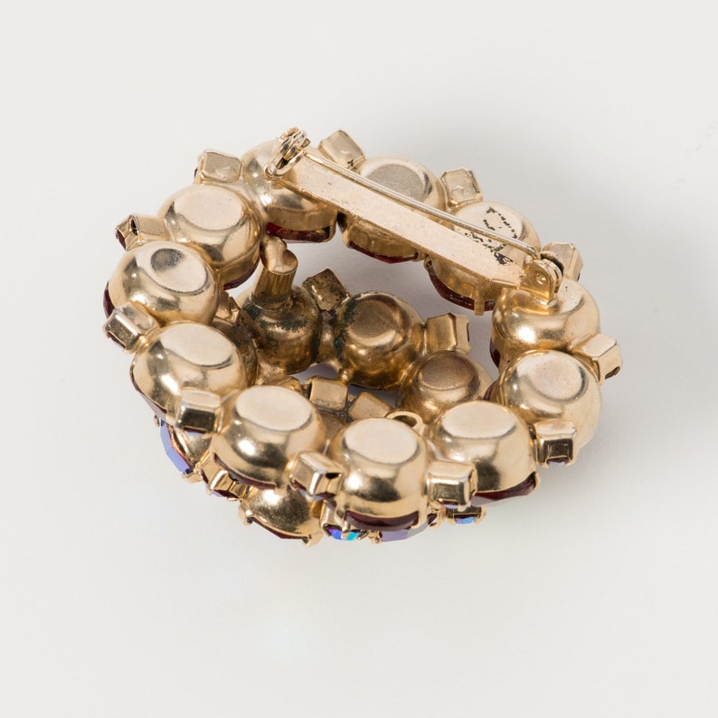 Puede incluir: Un broche dorado con un dise&ntilde;o circular adornado con piedras de imitaci&oacute;n rojas y azules.