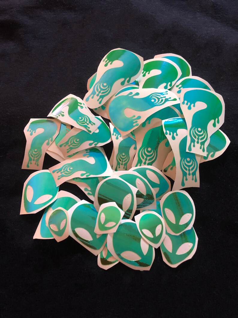 May include: A pile of green and blue holographic stickers featuring alien head and dripping liquid designs.