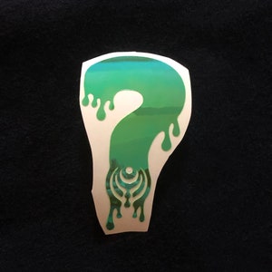 May include: A green and blue sticker with a dripping question mark design. The question mark has a stylized pattern inside.