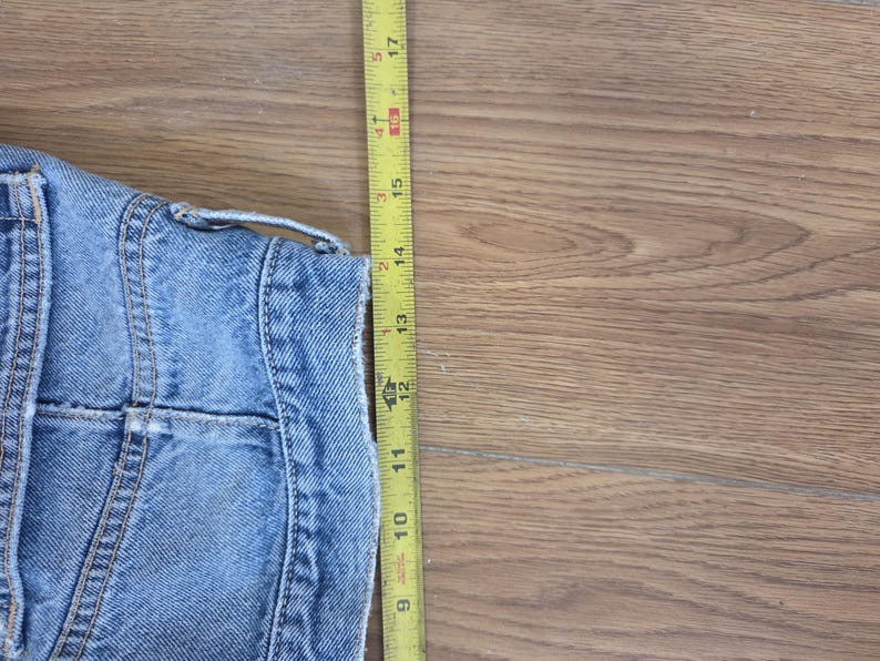 May include: A light blue denim jacket with a yellow measuring tape. The jacket's length is approximately 14 inches. The tape shows measurements in inches, with the jacket's details visible.