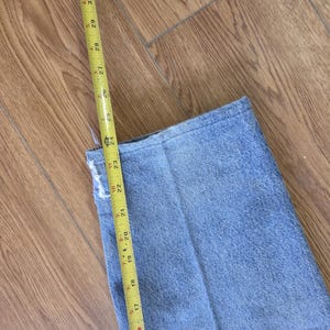 May include: A pair of light blue denim jeans with a yellow measuring tape showing a length of approximately 23 inches. The jeans are folded, and the tape is positioned along the edge, indicating a measurement.
