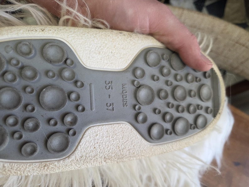 Puede incluir: Primer plano de la suela de un zapato, con una suela de goma gris texturizada con patrones circulares de varios tama&ntilde;os. La parte superior del zapato es blanquecina. La talla 35-37 es visible.
