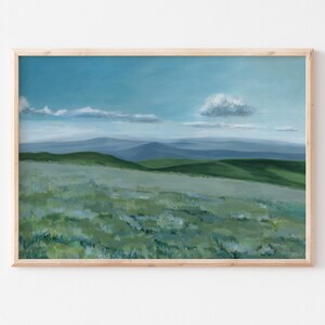 May include: A framed painting of a landscape with rolling green hills and a blue sky with white clouds. The painting is in a light wood frame.