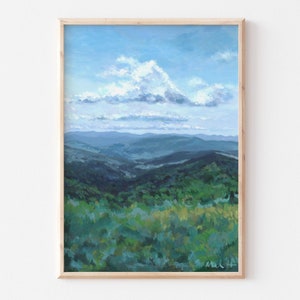 May include: A framed painting of a landscape with a blue sky and white clouds. The painting shows a view of rolling green hills and mountains in the distance.
