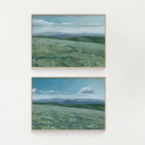 May include: Two framed landscape paintings with a blue sky and green hills. The top painting has a light blue sky with a few white clouds. The bottom painting has a darker blue sky with a single white cloud.
