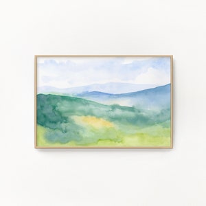 May include: Watercolor painting of a landscape with green hills and a blue sky. The painting is framed in a light wood frame.