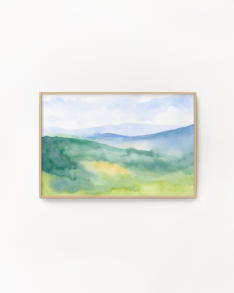 May include: Watercolor painting of a landscape with green hills and a blue sky. The painting is framed in a light wood frame.
