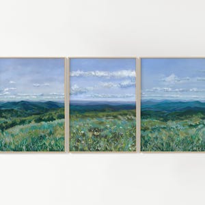 May include: A triptych of paintings depicting a landscape with rolling green hills and a blue sky with white clouds. The paintings are framed in wood.