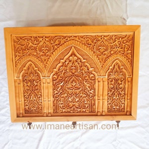 Peut inclure: Un panneau mural en bois avec des motifs sculptés complexes de couleur brun clair. Le motif présente trois ouvertures cintrées avec des motifs floraux et géométriques. Le panneau est encadré d'une simple bordure.