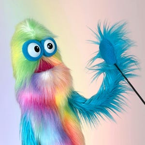May include: A colorful puppet with a rainbow-colored body and large, googly eyes. The puppet has a blue, feathery appendage extending from its arm. The puppet's mouth is open, revealing a pink interior. The puppet is designed for entertainment.