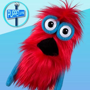 May include: A red puppet with large blue-rimmed eyes and a black mouth. The puppet has a shaggy texture and blue arms. A sign that reads "Puppet Layne" is in the upper left corner.