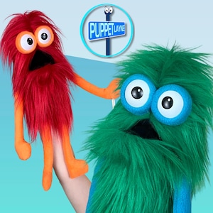 May include: Two colorful hand puppets. One is red with orange arms and legs, the other is green with blue eyes. A sign that says "Puppet Layne" is in the background.