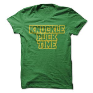 May include: Green t-shirt with the text "Knuckle Puck Time" in yellow letters.