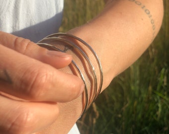 May include: Four gold-toned bangles stacked on a person's wrist. The bangles are smooth and shiny.