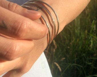 May include: A set of four gold-toned bangles stacked on a person's wrist. The bangles are smooth and have a slightly hammered texture.