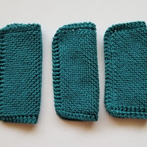May include: Three teal knitted washcloths with rounded corners. The washcloths are made with a textured knit stitch and have a finished edge. The washcloths are arranged vertically, with the largest on the left and the smallest on the right.