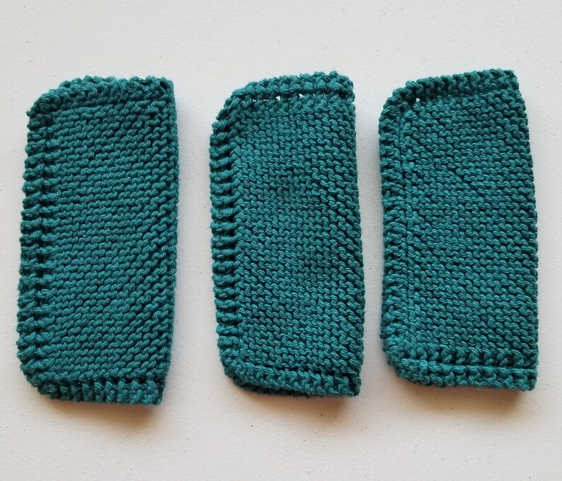 May include: Three teal knitted washcloths with rounded corners. The washcloths are made with a textured knit stitch and have a finished edge. The washcloths are arranged vertically, with the largest on the left and the smallest on the right.