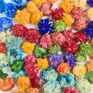 Könnte beinhalten: Eine Sammlung getrockneter Blumen in einer lebendigen Farbpalette aus Blau, Gelb, Rot, Orange, Grün und Violett. Jede Blume weist dichte, geschichtete Blütenblätter mit einer strukturierten Oberfläche auf, die dicht im Bild verteilt sind.