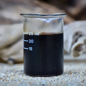 Può includere: Un becher di vetro trasparente con un liquido nero al suo interno. Il becher è contrassegnato con le misure di 15, 20 e 25 millilitri.