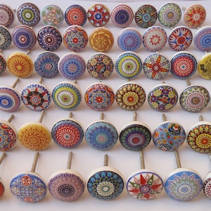 May include: A collection of 40 colourful ceramic cabinet knobs with intricate mandala designs. The knobs are white with a variety of colours, including red, blue, yellow, green, and orange. Each knob has a silver screw.
